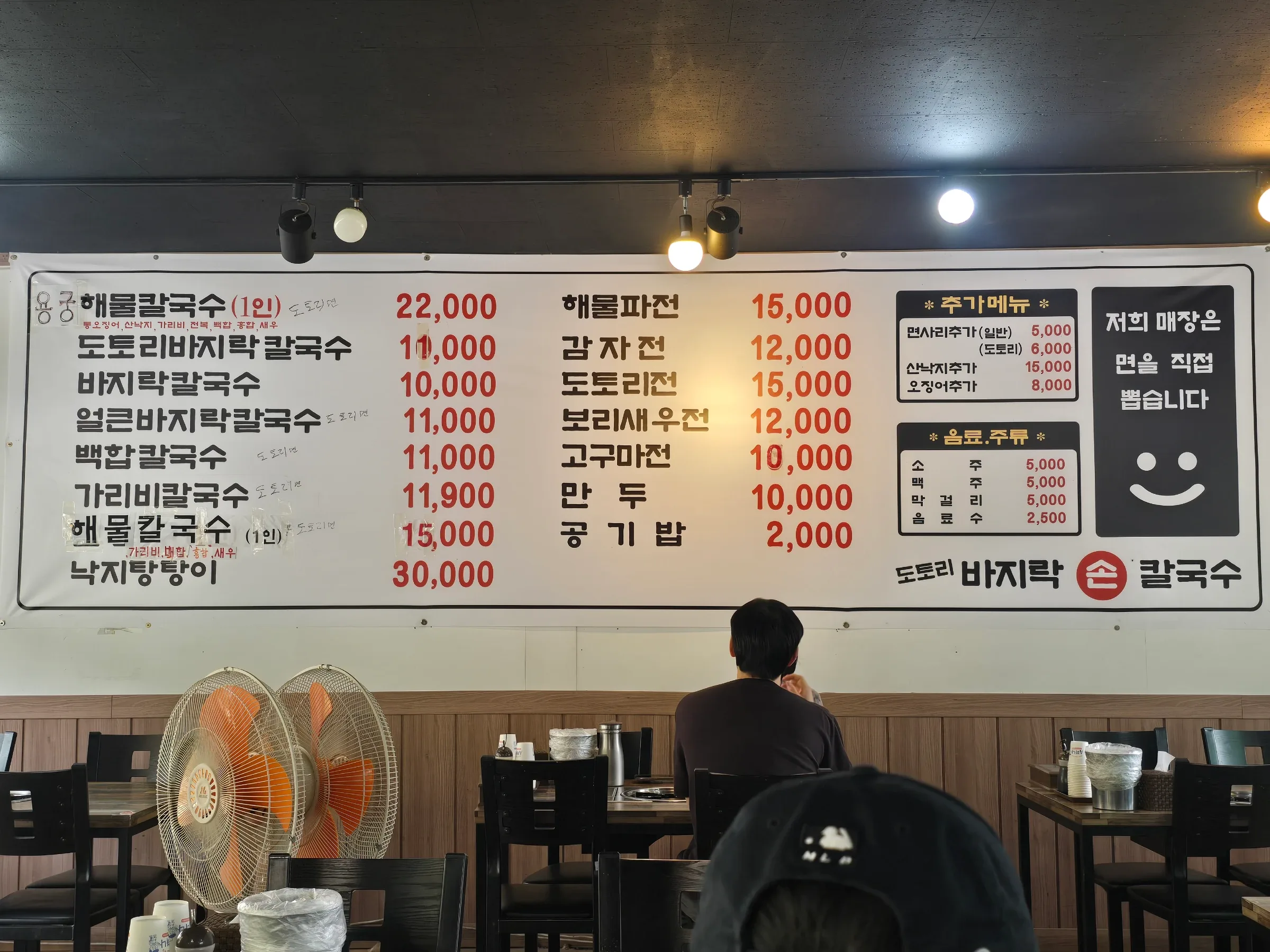A wall menu lists Yongwang Haemul Kalguksu for ₩22,000 above restaurant tables and seated diners.