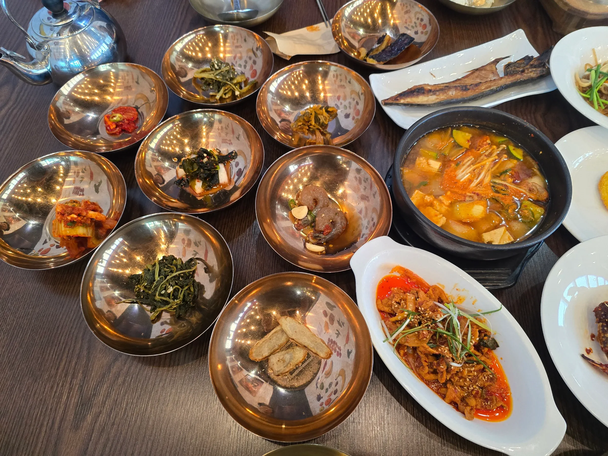 Brass bowls of banchan, a bubbling tofu and vegetable stew, grilled fish and a spicy stir-fried pork dish on a dark wooden table