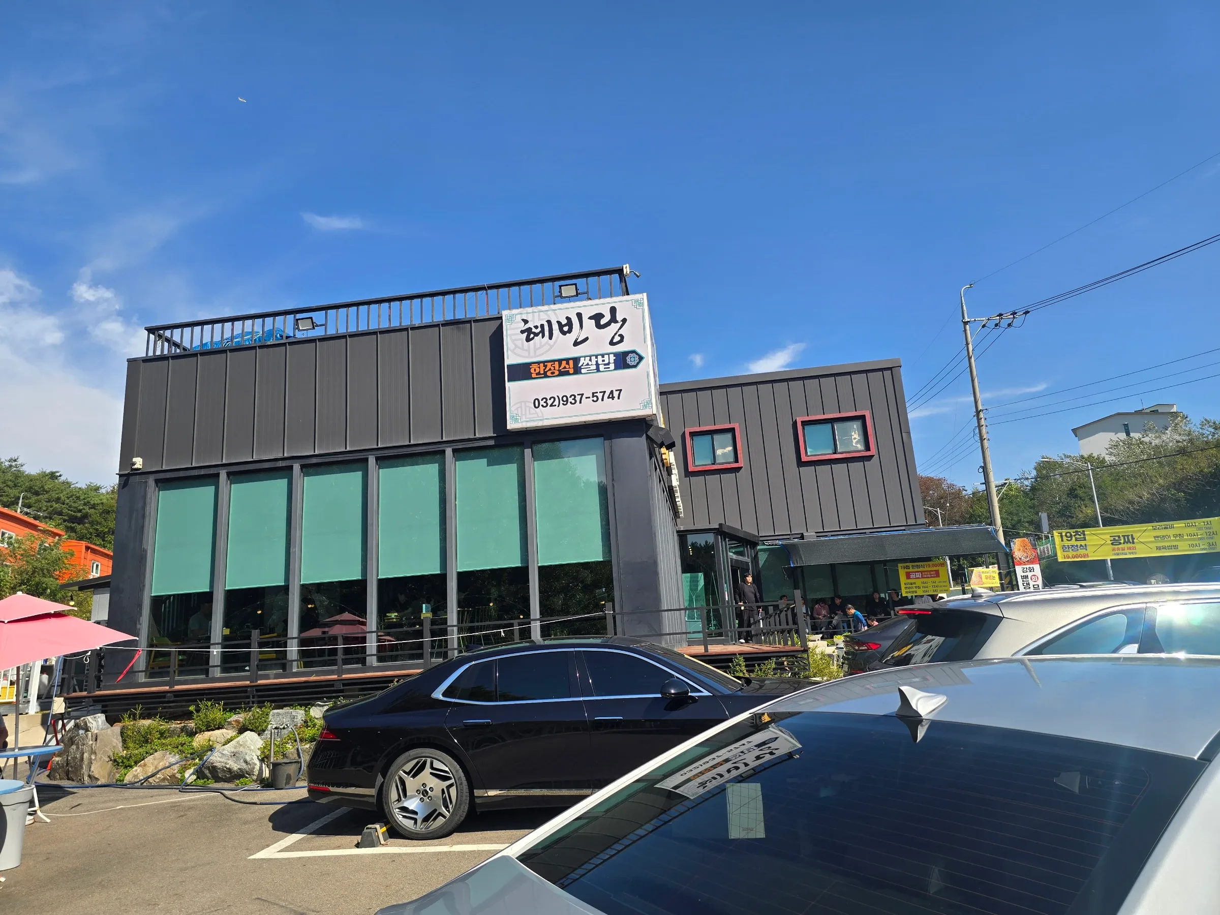Dark two-story restaurant with green window shades and a white sign reading 혜빈당 한정식 쌀밥, seen from a parking lot with cars.